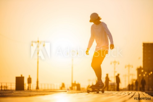 Picture of Silhouette of young boy riding longboard on the boardwalk summer time sunset